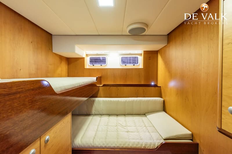 Een kajuit met houten wanden en twee bedden, waarvan één stapelbed, en twee patrijspoorten. — Jetten Custom