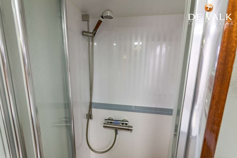 Een witte douchecabine met een glazen deur, een douchekop en een thermostaatkraan.