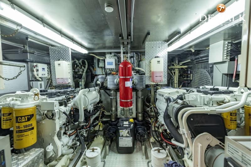 De foto toont een machinekamer met twee grote motoren, een rood brandblussysteem en diverse leidingen en filters.