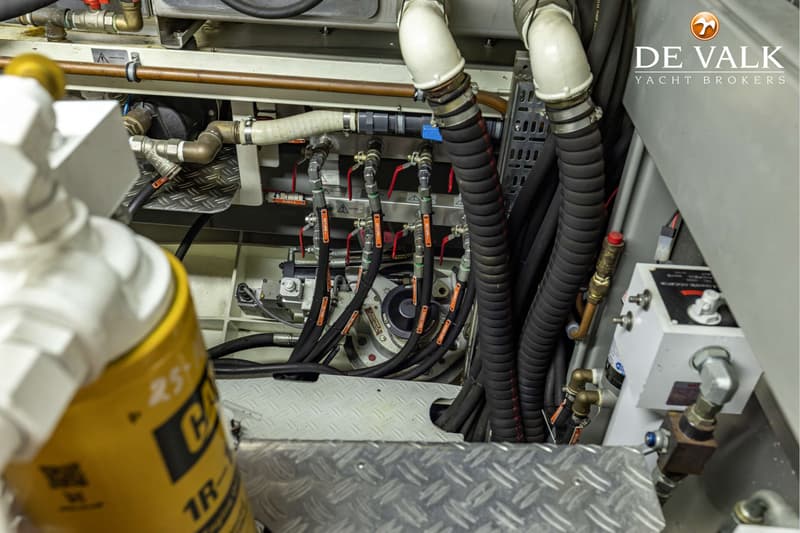 Een detailfoto van de motorruimte met diverse leidingen, kranen en een geel filter.