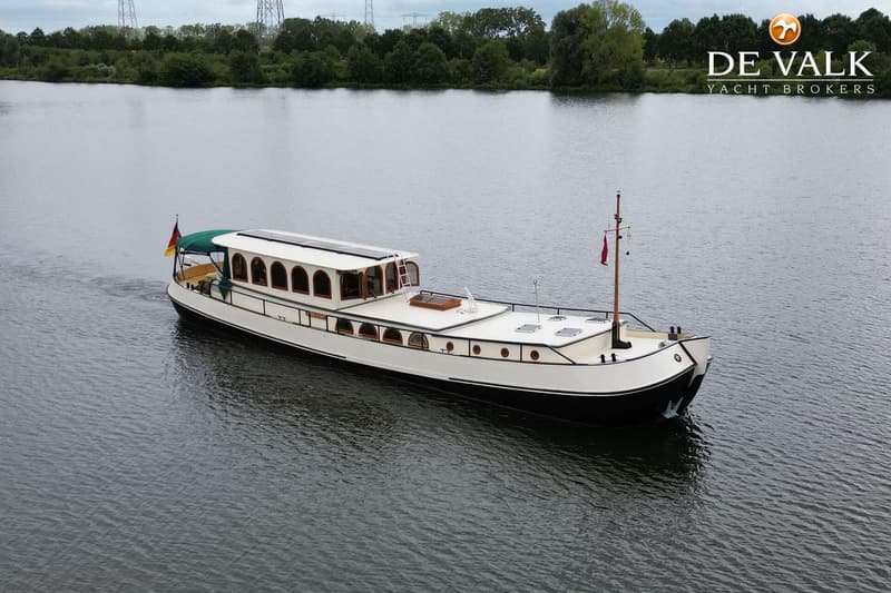 Een witte boot met een zwarte romp vaart op het water, met een Duitse vlag aan de achtersteven en een rode vlag aan de mast.