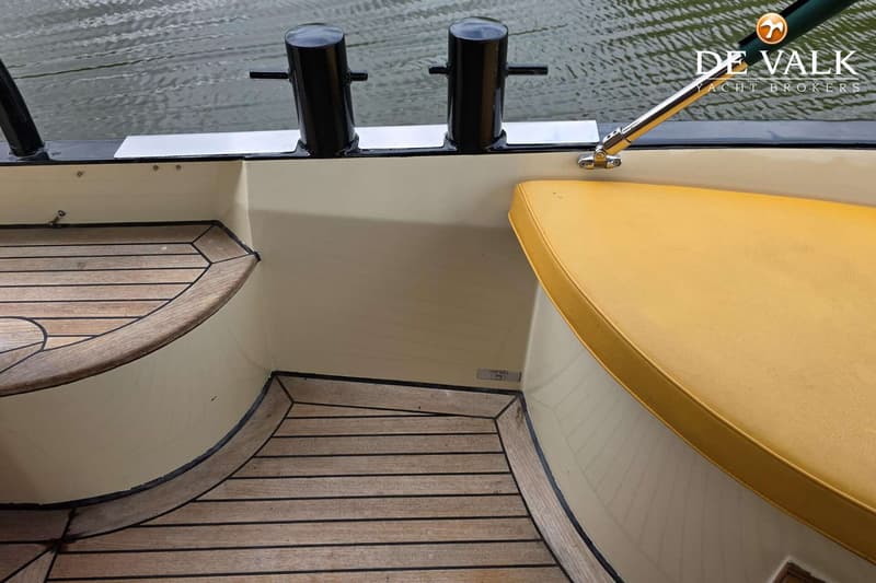 De foto toont een deel van een boot met een teakhouten vloer, een geel kussen en twee zwarte bolders. — Luxe motor 1900