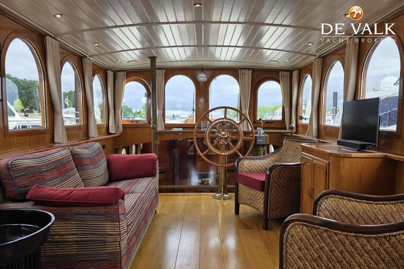 De foto toont het interieur van een boot met een houten stuurwiel, bank, rieten stoelen en een televisie. — Luxe motor 1900