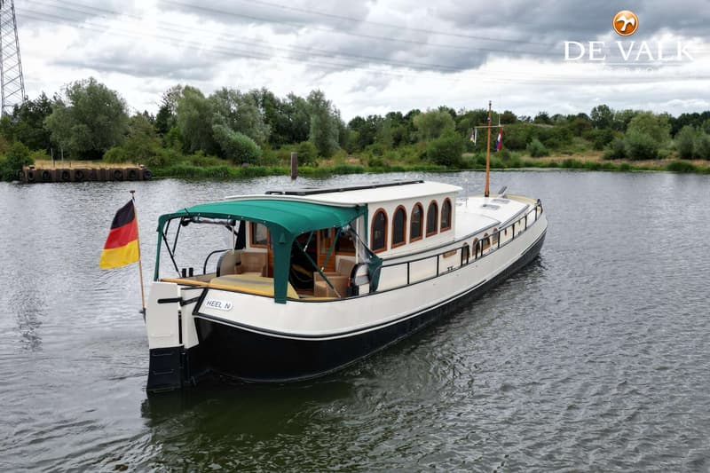 Een witte boot met een zwarte romp en een groene bimini vaart op een rivier onder een bewolkte hemel. — Luxe motor 1900