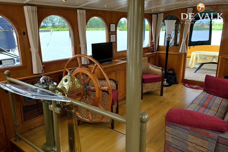 Een houten interieur van een boot met een stuurwiel, bank, stoelen en uitzicht op water. — Luxe motor 1900