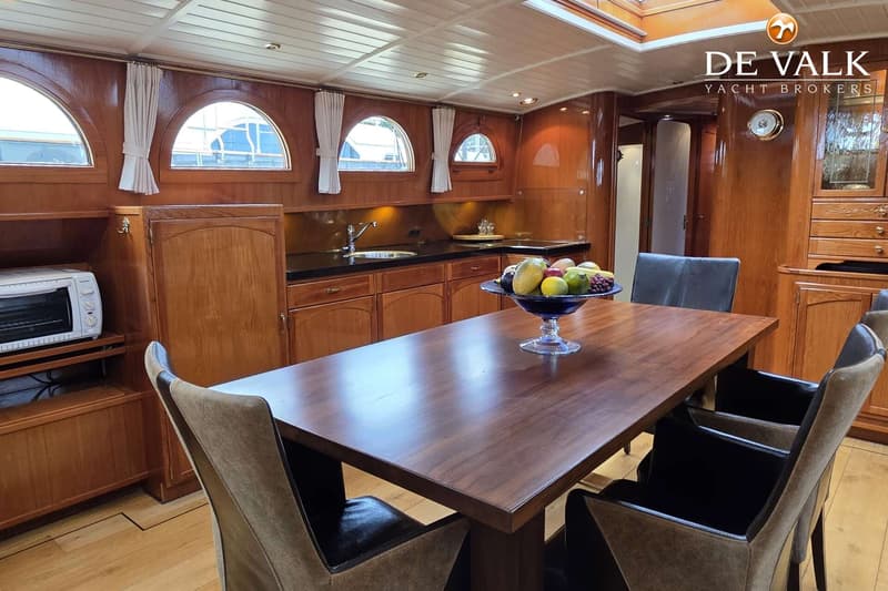Een houten interieur van een boot met een eettafel, stoelen, een kombuis en ramen met gordijnen. — Luxe motor 1900