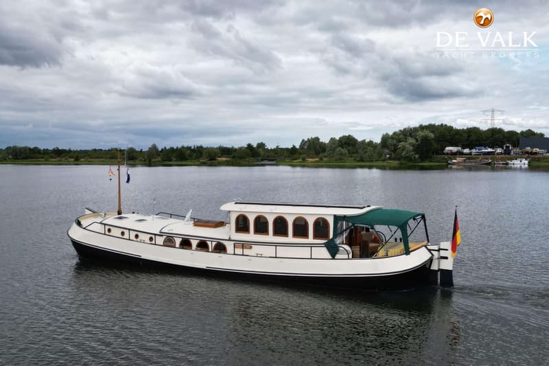 Een witte boot met zwarte romp vaart op een meer onder een bewolkte hemel, met een Duitse vlag aan de achtersteven.