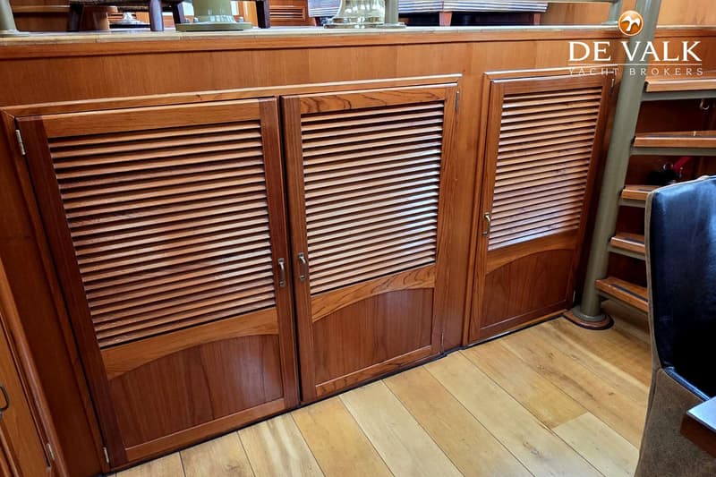 Drie houten kasten met lamellen deuren en handgrepen, een houten vloer en een trap met een leuning.