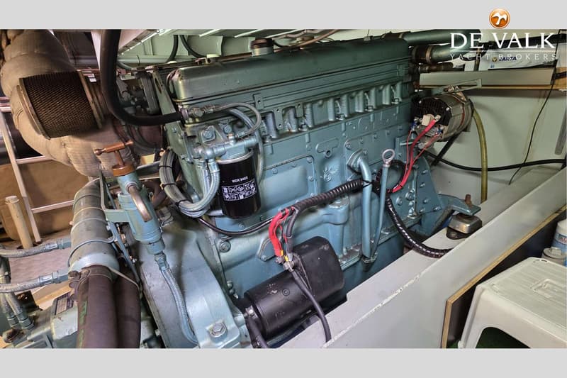 Een close-up van een blauwgroene scheepsmotor met diverse leidingen, kabels en een zwart oliefilter.