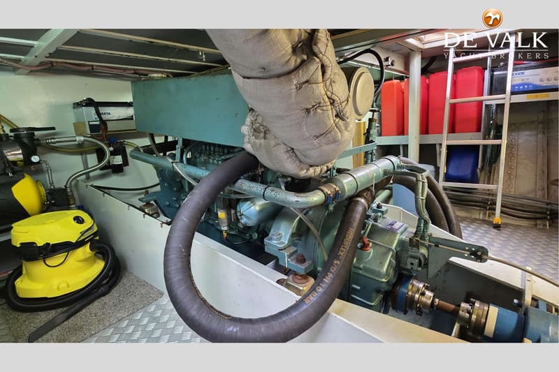 Een detailfoto van een scheepsmotor met diverse slangen, een Varta accu, een gele stofzuiger en rode jerrycans.