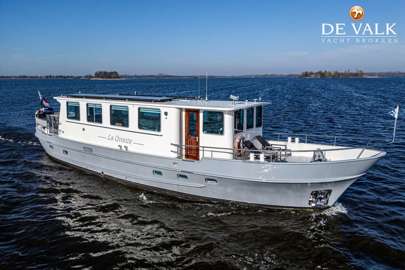 Een witte motorboot met de naam "La Qrooze" vaart op open water onder een heldere blauwe lucht.