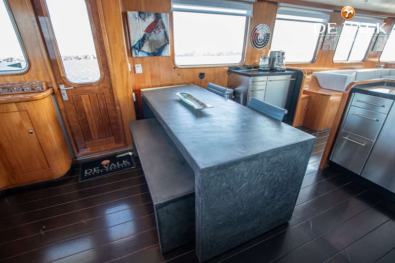 Een interieur van een boot met houten wanden en vloer, een donkere tafel met bank, en een keukenblok.