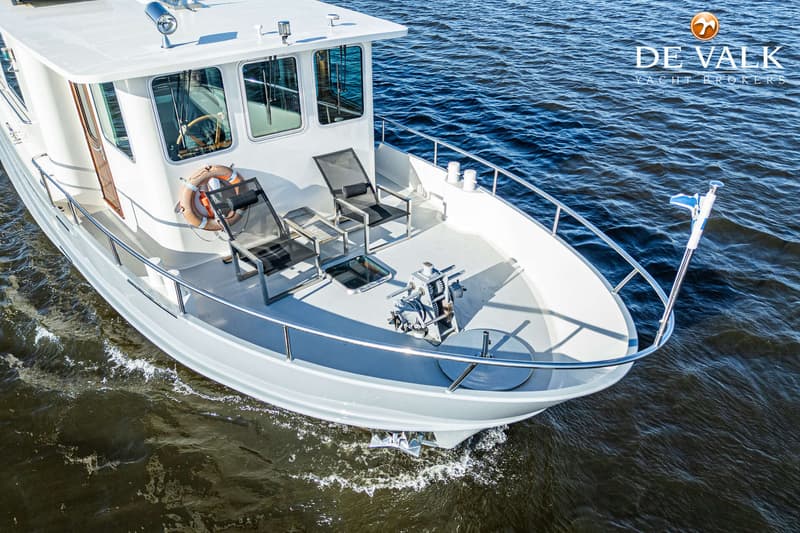 Een witte motorboot met een stuurhut, twee ligstoelen en een ankerlier op het voordek, vaart op het water.