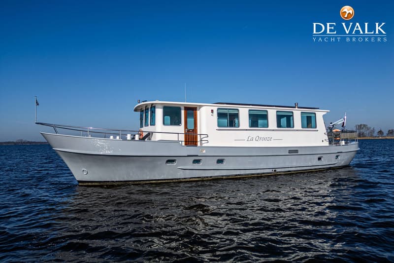 Een grijze en witte motorboot met de naam "La Qrooze" vaart op open water onder een heldere blauwe lucht.