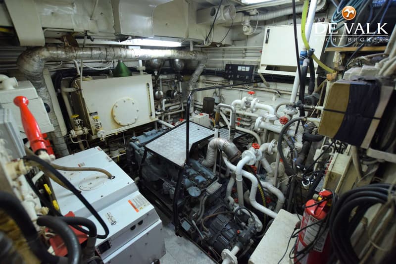 Een overzicht van een machinekamer met een grote motor, diverse leidingen, kleppen en een brandblusser.