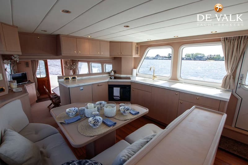 Een interieur van een boot met een keuken, eettafel en zitbanken, met uitzicht op water en land.