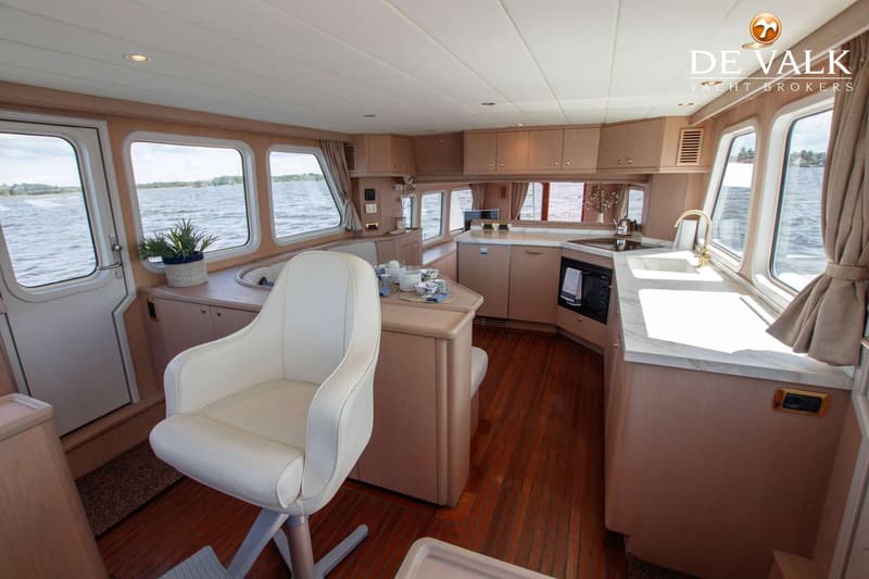 De foto toont het interieur van een boot met een keukenblok, een eettafel en een witte stoel, met uitzicht op water.