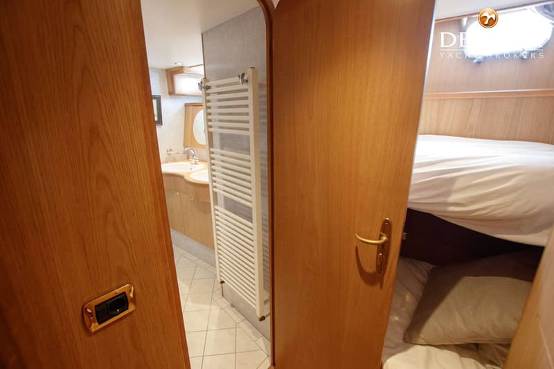 Een interieurfoto met een badkamer met twee wastafels en een handdoekradiator, en een slaapcabine met een bed.