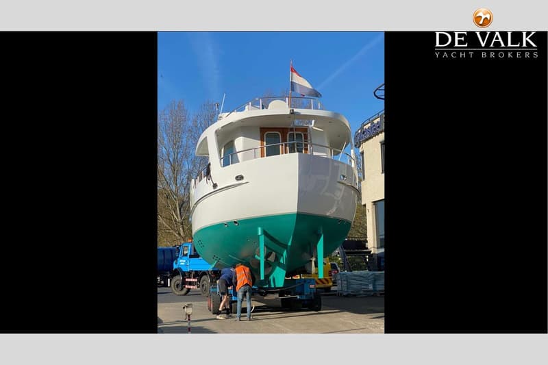 Een witte boot met een turquoise onderkant staat op een trailer, met twee mensen die eraan werken.