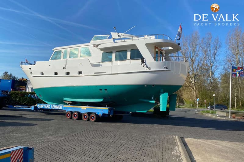 Een witte boot met een turquoise onderkant staat op een blauwe trailer met "SHIPYARD LEMMER" erop, onder een blauwe lucht.