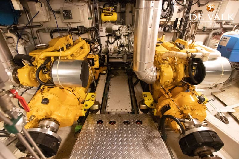De foto toont een machinekamer met twee grote gele motoren aan weerszijden van een metalen loopbrug.
