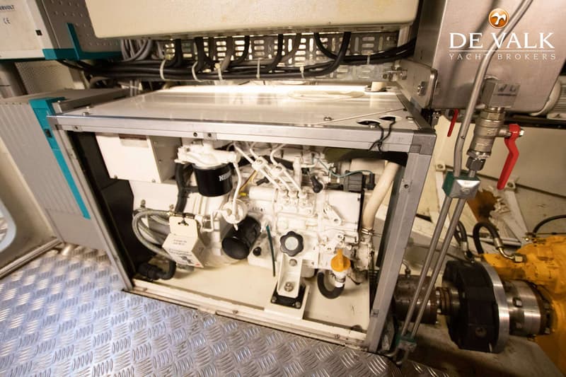 Een witte motor met zwarte en gele onderdelen is zichtbaar in een open compartiment op een metalen vloer.