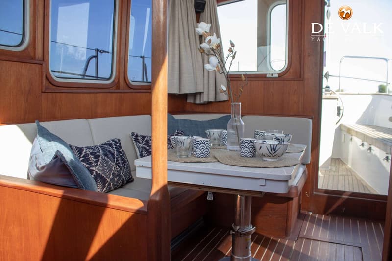Een interieur van een boot met houten wanden, ramen, een bank met kussens en een tafel met servies.