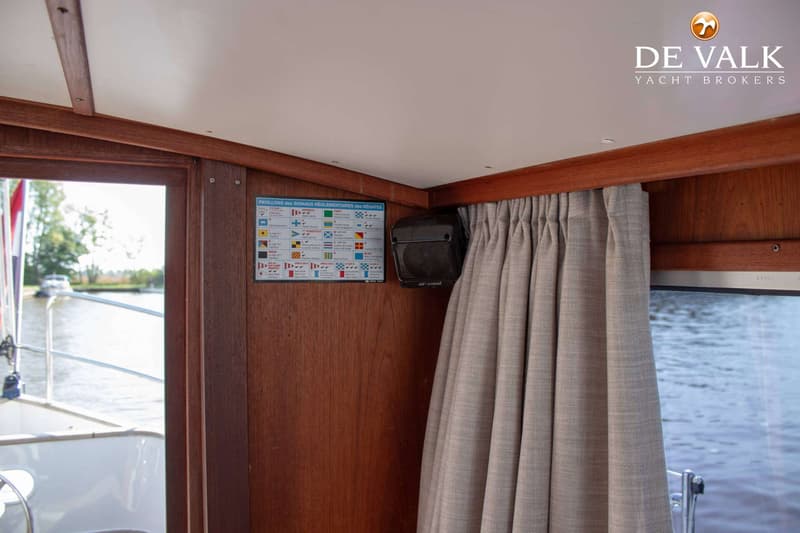 Een interieur van een boot met houten wanden, een wit plafond, een gordijn, een speaker en een overzicht van vlaggen.