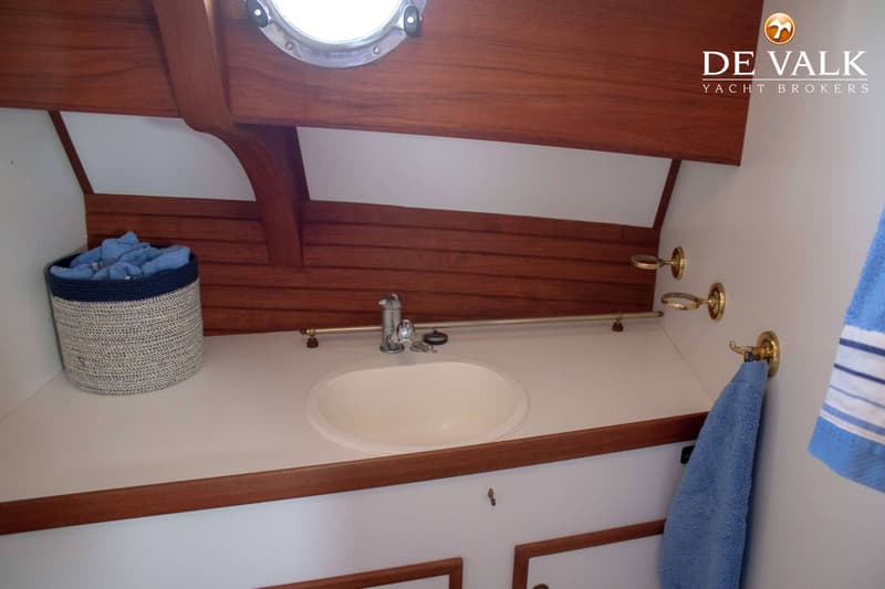 Een badkamer met een wastafel, kraan, handdoeken, een patrijspoort en houten afwerking.