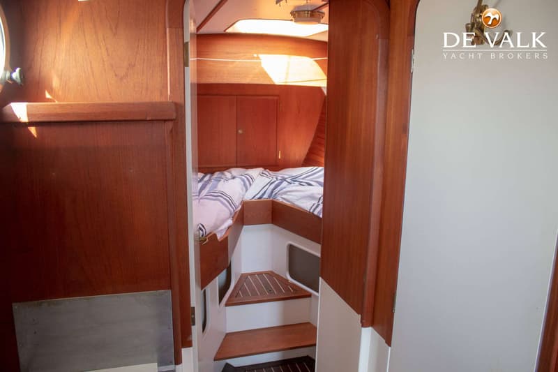De foto toont een kajuit met een bed, houten wanden, een trapje en het logo van De Valk Yacht Brokers.