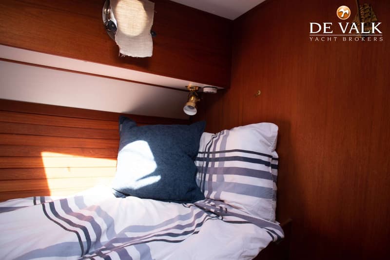 Een kajuit met een bed met gestreepte dekens en twee kussens, omringd door houten panelen en een leeslampje.