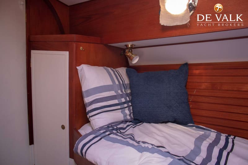 Een bed met gestreepte kussens en dekbed, een blauw kussen, en houten lambrisering met een leeslampje.