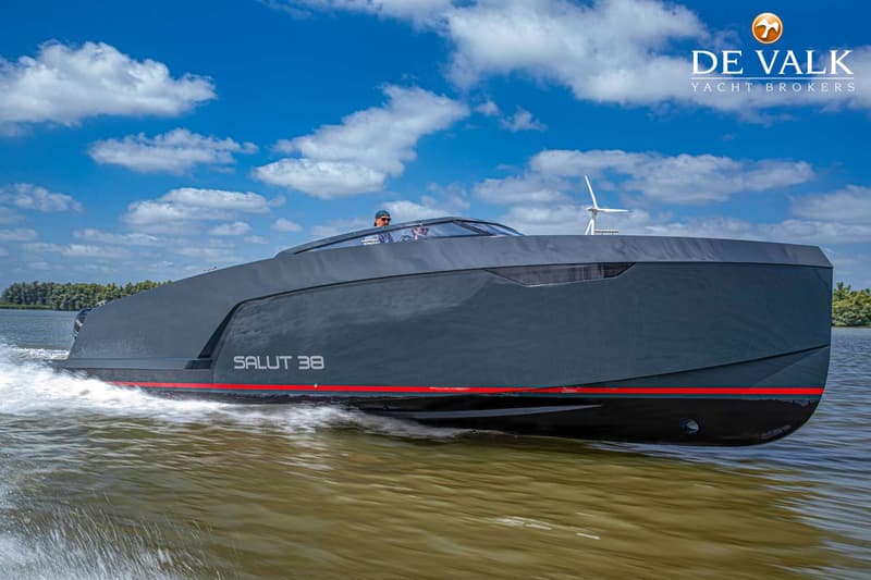 Een donkergrijze motorboot met de tekst "SALUT 38" en een rode streep op de zijkant vaart over water. — Salut 38
