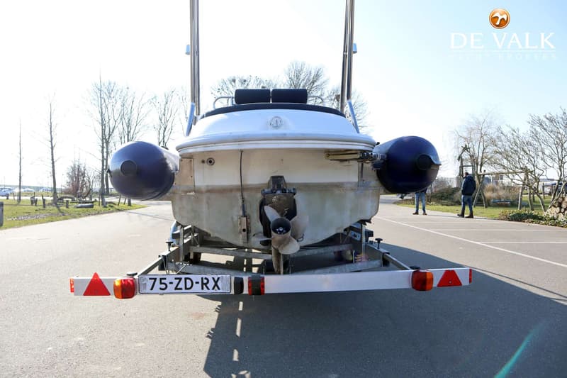 Een witte boot met een buitenboordmotor en twee blauwe stootwillen, staat op een trailer met kenteken 75-ZD-RX.