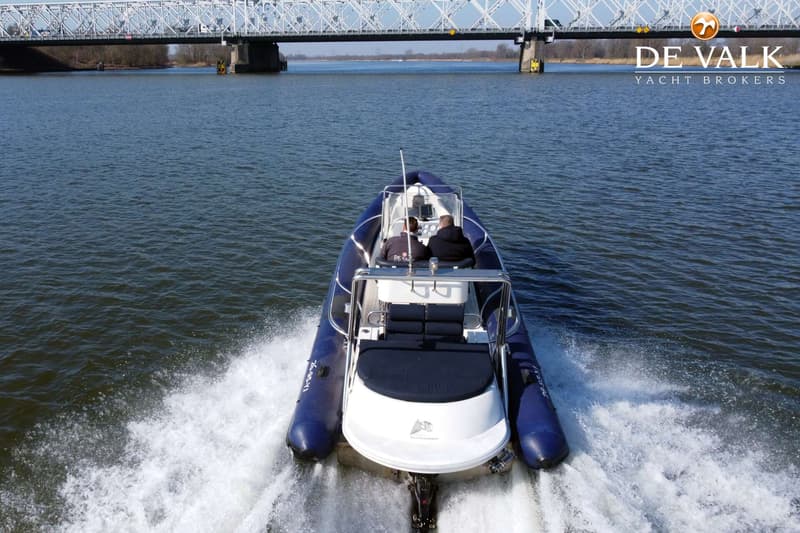 Een blauw-witte RIB-boot met twee personen aan boord vaart over water, met een brug op de achtergrond. — Arctic Blue 27