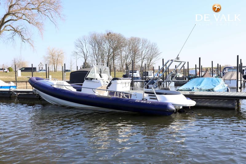 Een witte RIB met een donkerblauwe tube ligt afgemeerd aan een steiger in een jachthaven.