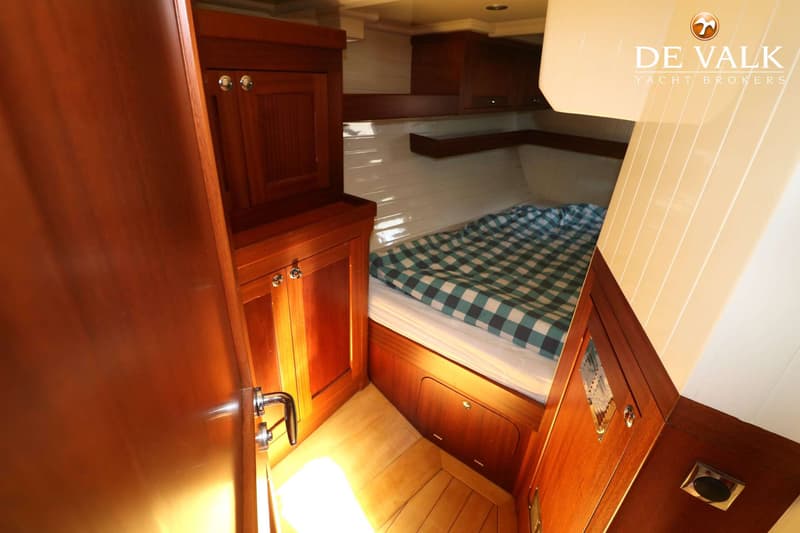 Een kajuit met een bed met een geruit dekbed, houten kasten en een houten vloer. — Bestewind 50 Pilothouse