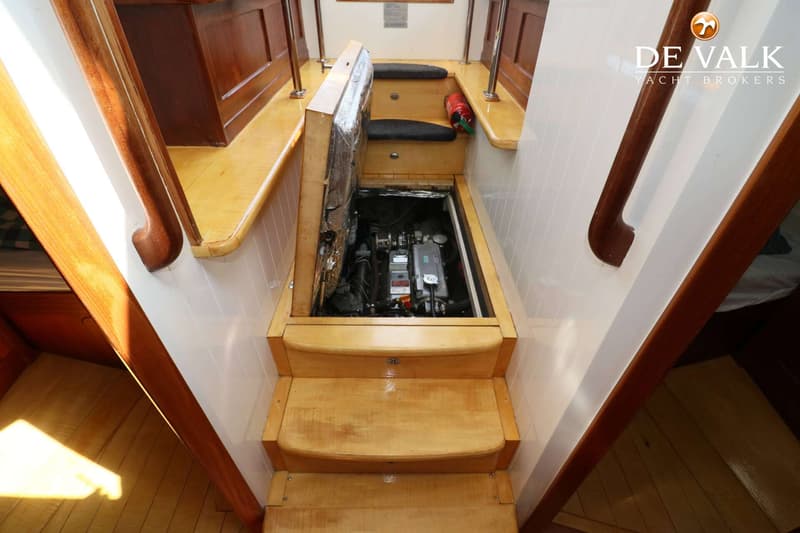 Een houten trap met drie treden leidt naar beneden, met een open luik dat een motorcompartiment onthult.