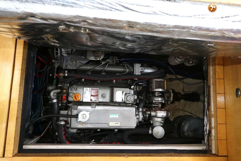 Een close-up van een scheepsmotor in een afgesloten ruimte met houten panelen en isolatiemateriaal.