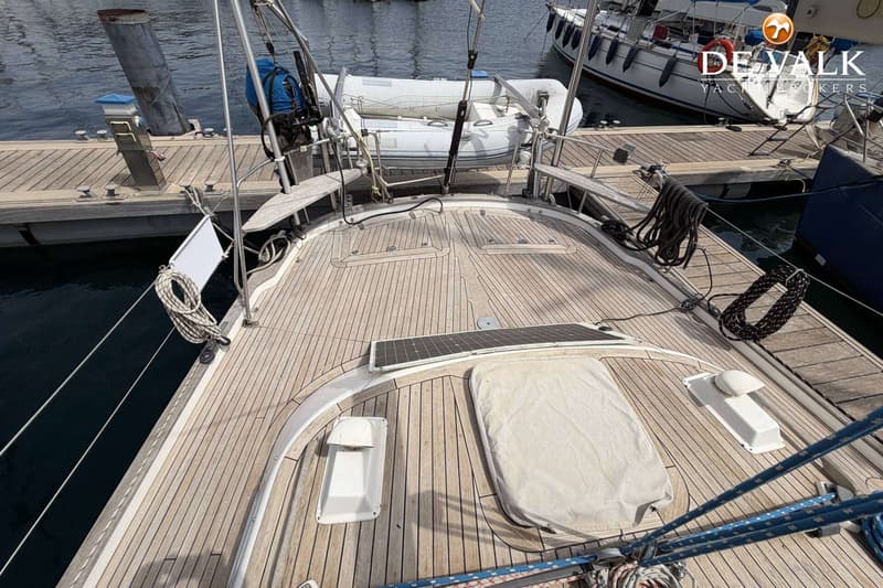De foto toont het teakhouten dek van een zeilboot met een zonnepaneel, touwen en een bijboot aan de achtersteven.