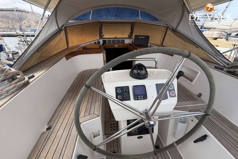 De foto toont het stuurwiel en de cockpit van een zeilboot, met navigatie-instrumenten en een kompas. — Hallberg Rassy 46