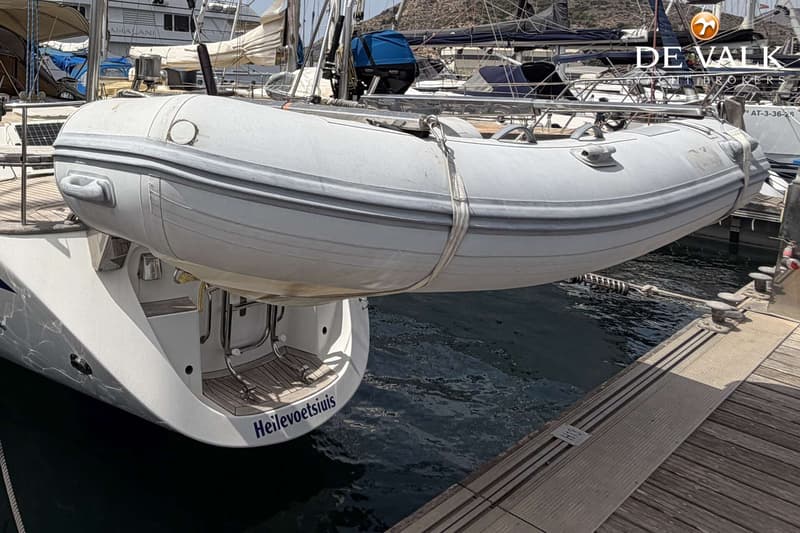 Een witte bijboot hangt aan davits boven het water, met de naam "Heilevoetsluis" op de spiegel van de boot eronder.