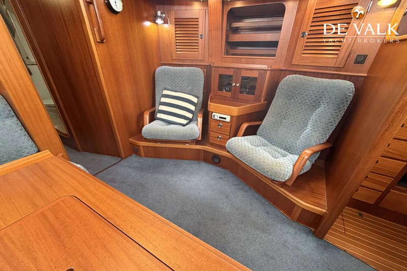 De foto toont een interieur van een boot met twee gestoffeerde stoelen, houten wanden en een grijs tapijt.