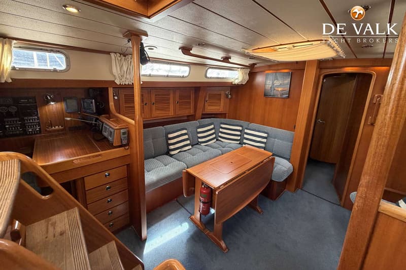 Een interieur van een boot met houten lambrisering, een blauwe bank met gestreepte kussens, een klaptafel en een…