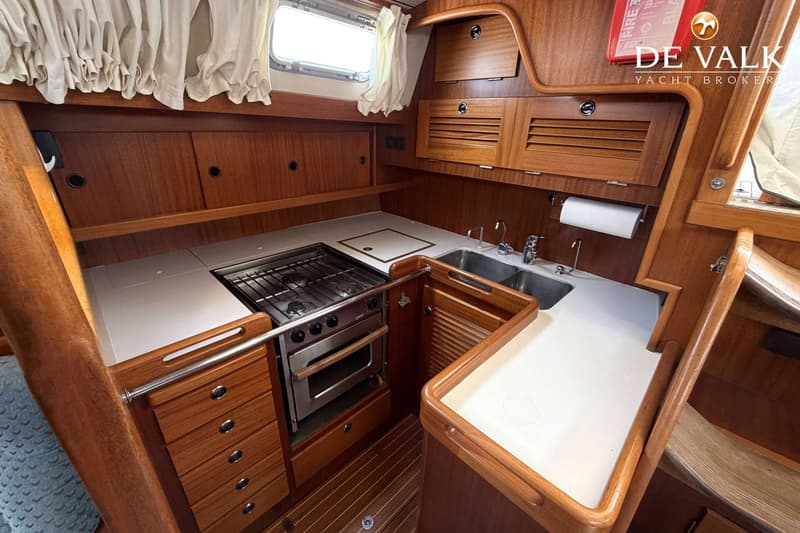 Een kombuis met een fornuis, oven, dubbele spoelbak, aanrecht en houten kasten.