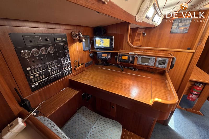 Een houten navigatiehoek met diverse elektronische apparatuur, schakelpanelen en een kussen.