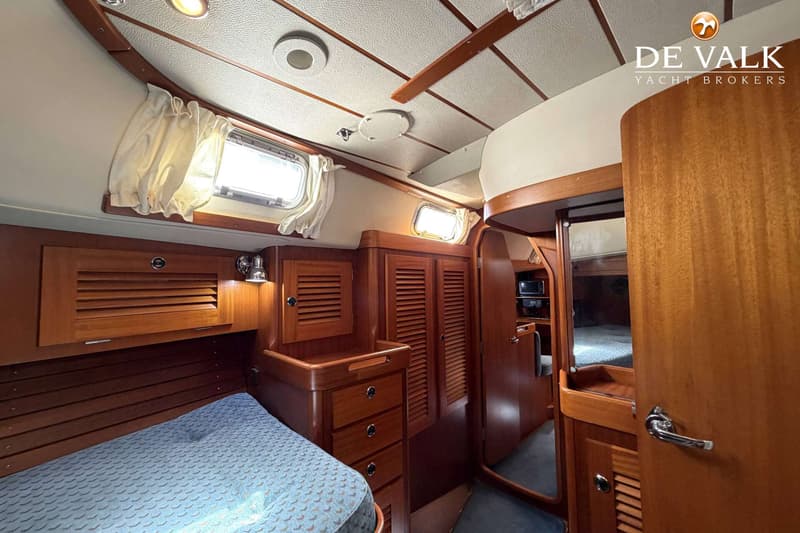 Een kajuit met een bed, houten kasten, laden, een spiegel, ramen met gordijnen en een plafond met verlichting.