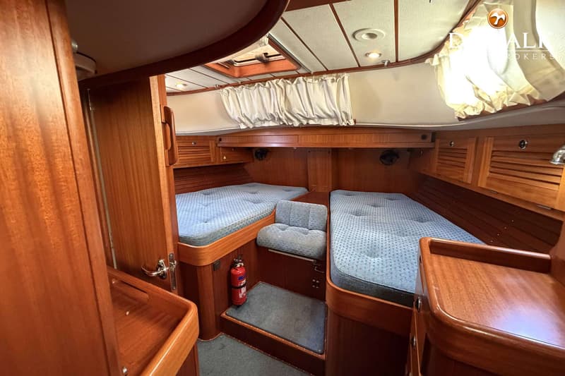 De foto toont een kajuit met twee bedden met blauwe matrassen, een brandblusser en houten kasten. — Hallberg Rassy 46
