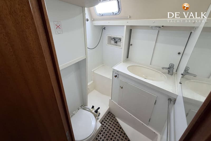 De foto toont een witte badkamer met een toilet, wastafel, spiegel en een douchekop.
