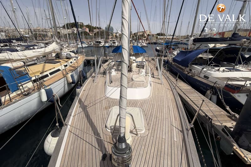 Een bovenaanzicht van het teakhouten dek van een zeilboot, met de mast en opgerolde zeilen in het midden. — Hallberg Rassy 46